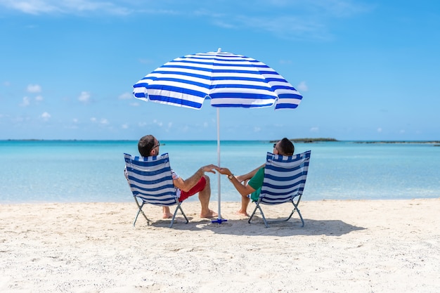 Männer sitzen in Stühlen unter Sonnenschirm an einem tropischen Strand