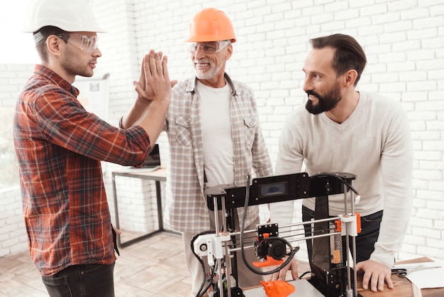 Männer stehen drei zusammen um den 3D-Drucker.