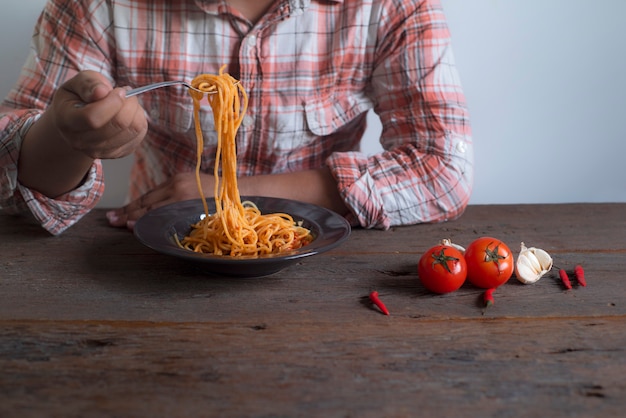 Männer tragen die Hemden, die einen Spaghetti mit einem Löffel halten, der auf einen Holztisch gesetzt wird