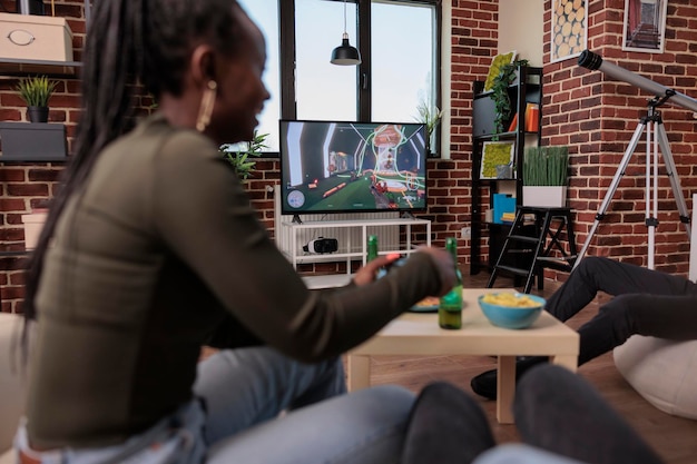 Foto männer und frauen spielen videospiele im fernsehen und genießen das schießspiel auf der konsole beim treffpunkt mit freunden. spaß mit shooter-strategie, freizeitbeschäftigung mit alkohol.