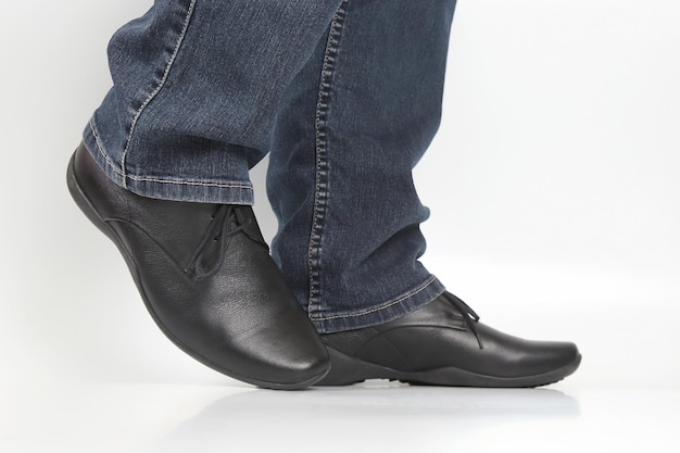 Männerbeine in Jeans und schwarzen klassischen Schuhen auf weißem Hintergrund