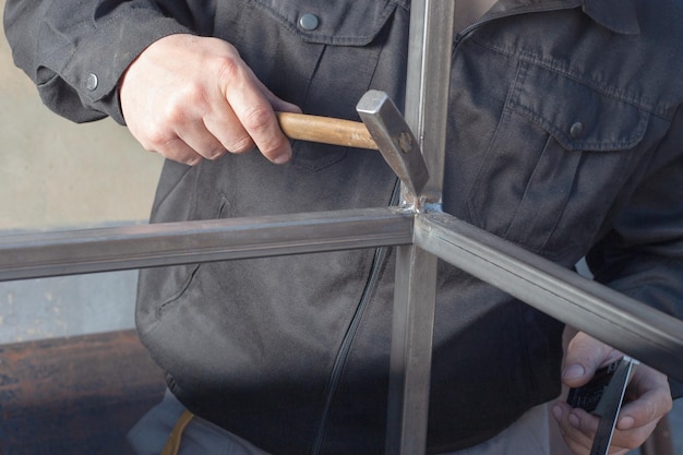 Männerhände mit einem Hammer, die nach dem Schweißen eines Metallprofils Überschuss abwehren