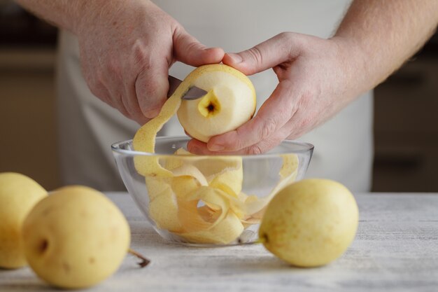 Männerhände schälen Birne. Mann schält Obst am Tisch. Süße Zutat für leckeres Essen.