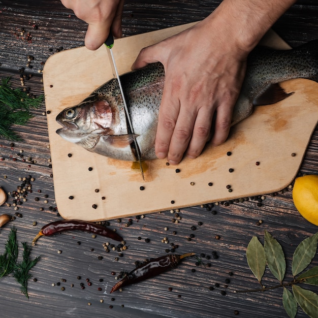 Männerhände schnitten rote Fische ins Brett