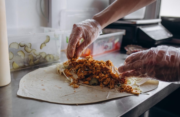 Männerhände wickeln traditionelle Shawarma-Wrap mit Hühnchen und Gemüse ein