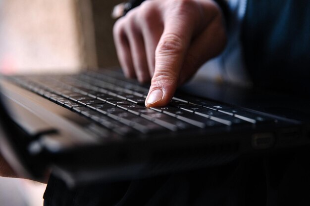 Männerhand, die auf einer Laptoptastatur tippt Selektiver Fokus