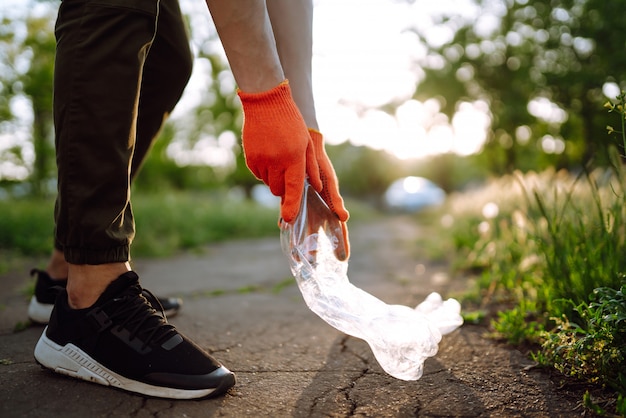 Männerhand sammelt Plastikmüll für die Reinigung im Park. Freiwillige, die Schutzhandschuhe tragen, sammeln Flaschenplastik.