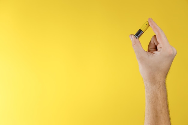 Männlich halten graugelbe AA-Alkalibatterie auf gelbem Hintergrund Recycling von wiederaufladbaren Batterien