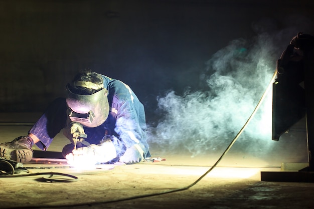 Männliche Arbeiter, die Schutzkleidung tragen, reparieren Bodenplatte Lagertank Industriebau Rauchscheinwerfer in engen Räumen.
