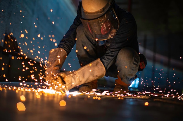 Männliche Arbeiter Metallschneidfunken auf der Stahlplatte des Tankbodens mit Blitzlicht, Nahaufnahme, Schutzhandschuhe und Maske in seitlich begrenztem Raum tragen.