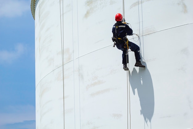 Männliche Arbeiter Seilzugangshöhensicherheitsinspektion der Dickenlageröl- und Gastankindustrie Wolkenblauer Himmel.