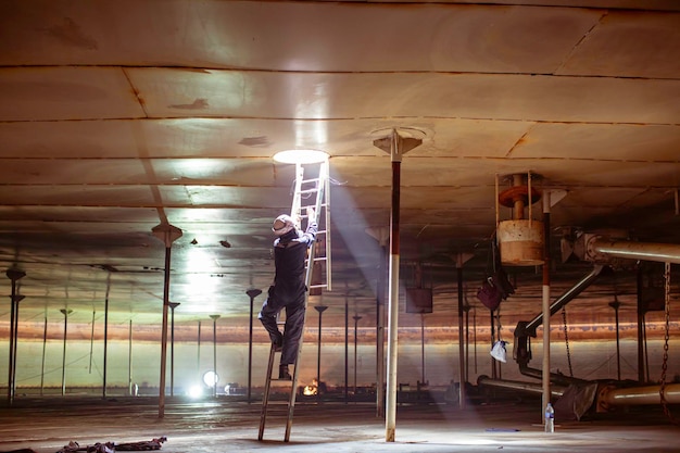 Männliche arbeiter steigen in den visuellen inspektionstank des treppenhauslagers in den engen raum ein, in dem die beleuchtung ist