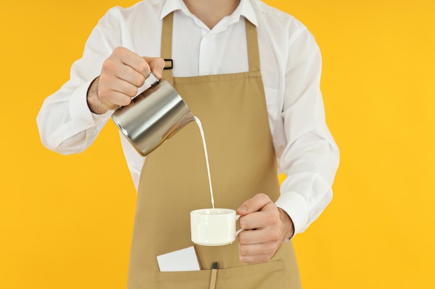 Männliche Barista gießen Milch auf gelbem Hintergrund