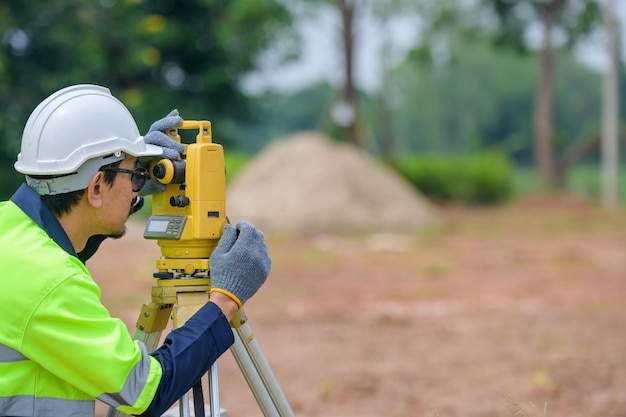 Männliche Bauingenieurvermessung mit Theodolitapparat Vor dem Bau auf der Baustelle von Straßen oder Gebäuden mit Baumaschinenhintergrund