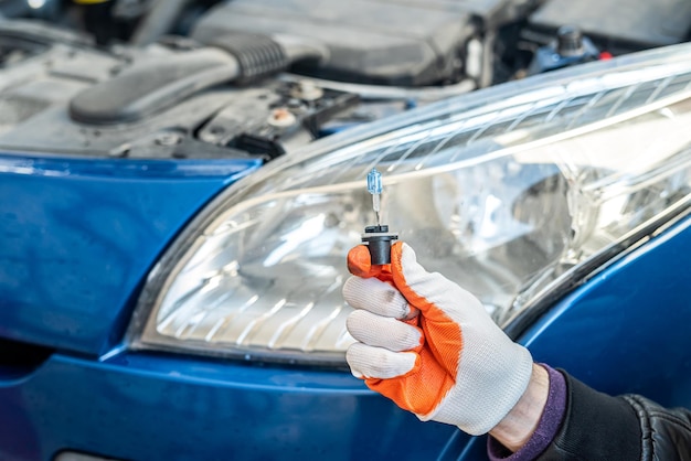 Männliche behandschuhte Hand hält eine Gelagon-Lampe auf dem Hintergrund eines Autoscheinwerfers Autoreparaturkonzept