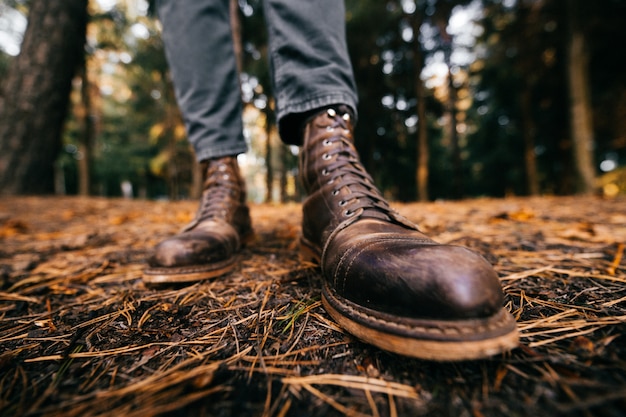 Männliche Beine, die stilvolle braune Lederstiefel im Herbstwald demonstrieren.