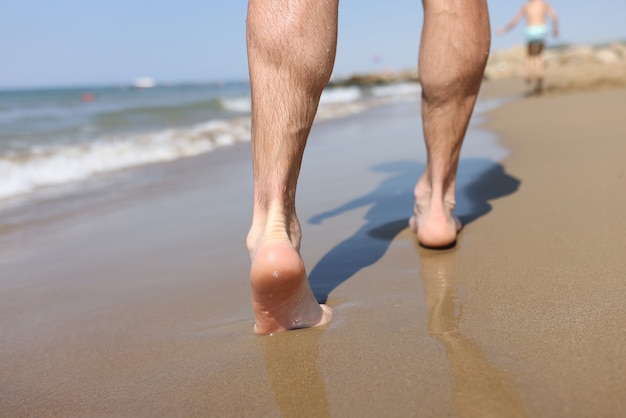 Männliche Füße, die auf Sand bei Strandnahaufnahme gehen