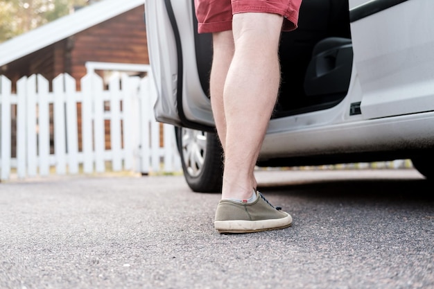 Männliche Füße in einem Turnschuh stehen neben einem Auto, das auf der Straße einer Provinzstadt im Hof in der Nähe des Zauns geparkt ist