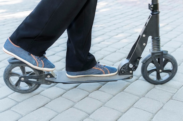 Männliche Füße in Turnschuhen und Hosen fahren einen Roller auf dem Bürgersteig und die Radbremsen, Nahaufnahme