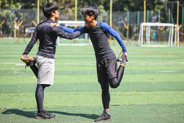 Männliche Fußballspieler, die sich vor dem Spiel auf der grünen Wiese die Beine zusammenstrecken
