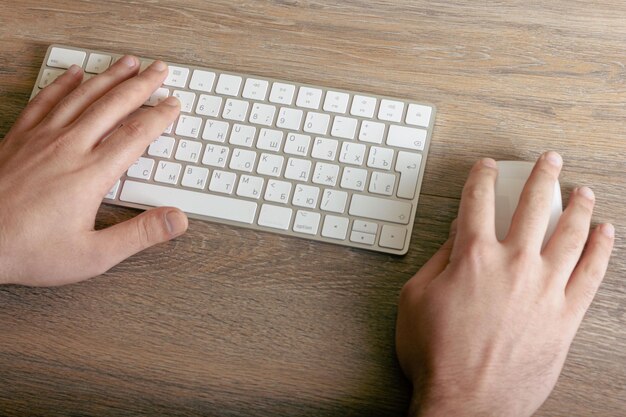 Männliche Hände an Tastatur und Maus auf einem Holztisch