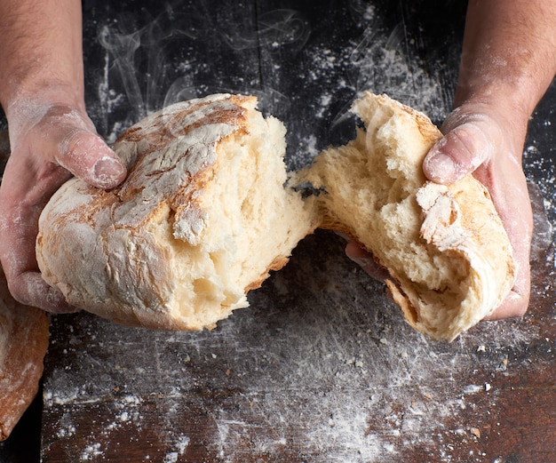 Männliche Hände, die aufgebackenes Brot zur Hälfte brechen