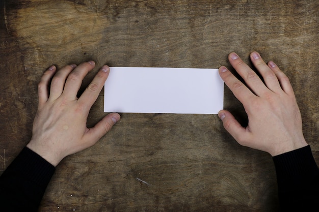 männliche Hände, die ein weißes leeres Blatt Papier auf dem Hintergrund des Holzstrukturtischs halten