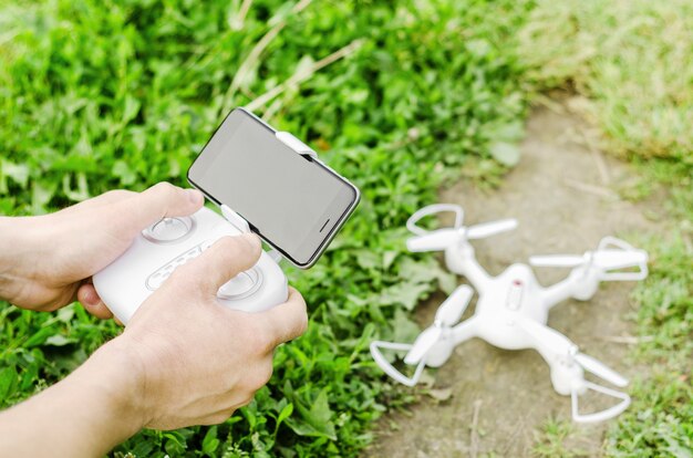 Männliche Hände, die eine Fernbedienung mit einem Smartphone von einem Quadrocopter auf dem Hintergrund von Gras und Drohne halten. Das Konzept der modernen Technologie, fliegen.