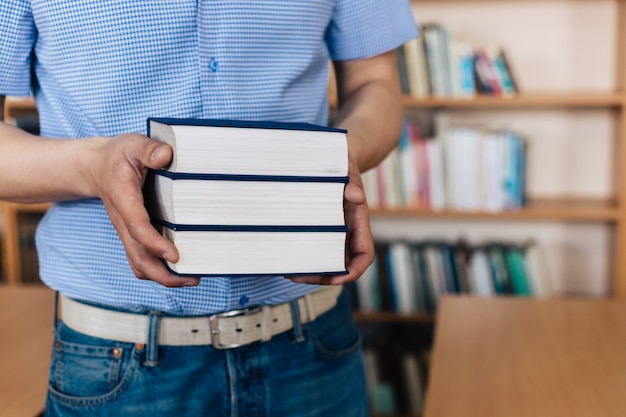 Männliche Hände, die einen Stapel Bücher halten.