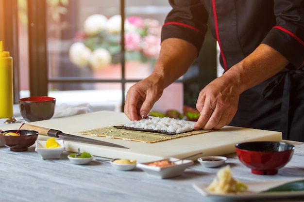 Männliche Hände, die Reis berühren Noriblatt mit weißem Reis. Das Rezept des Küchenchefs für Hosomaki-Brötchen. Arbeite in der Küche eines japanischen Restaurants.