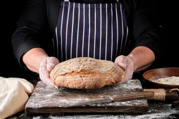 Männliche Hände halten braunes gebackenes Roggenbrot