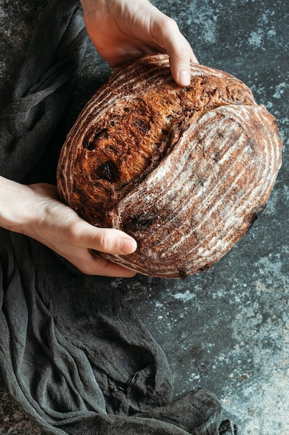 Männliche Hände halten hausgemachtes Brot auf dunklem Hintergrund. Brot mit Nüssen und kandierten Früchten.