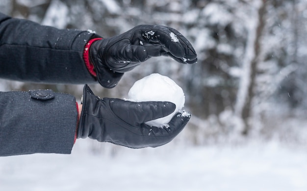 Foto männliche hände in handschuhen, die schneeball aus schnee im wald machen oder formen, schließen oben.