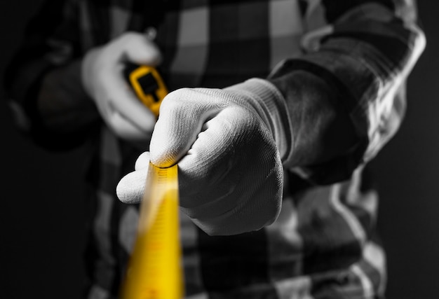 Männliche Hände in weißen Bauhandschuhen, die ein gelbes einziehbares Maßband halten, verteilen sich auf die Kamera, Nahaufnahme.
