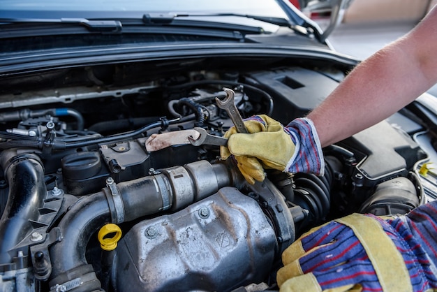 Männliche Hände mit Schraubenschlüsseln. Auto-Service-Konzept. Hände in Schutzhandschuhen gegen Automotor