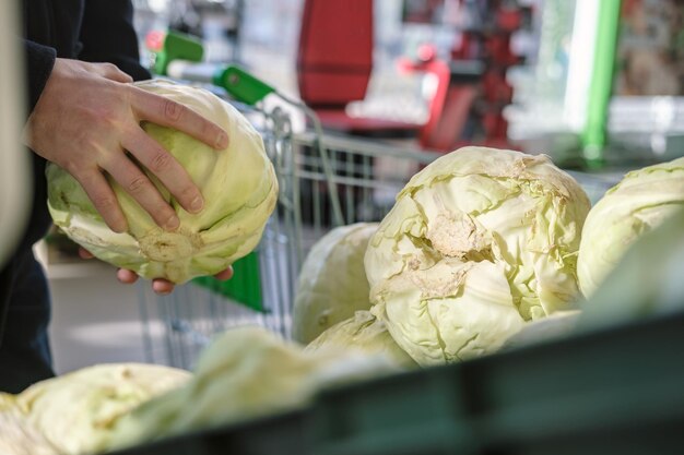 Männliche Hände nehmen frischen Kohl von der Theke mit Gemüse im Laden