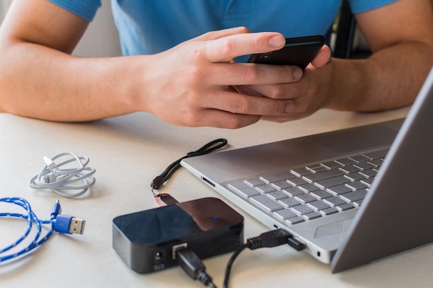 Männliche Hände prüfen das Mobiltelefon neben dem Laptop auf dem Schreibtisch. Selektiver Fokus