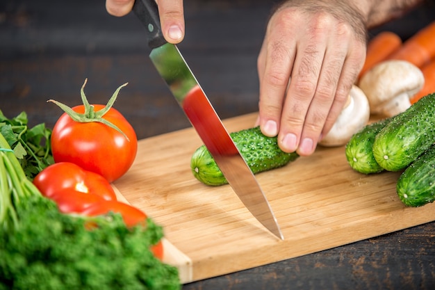 Männliche Hände schneiden Gemüse für Salat