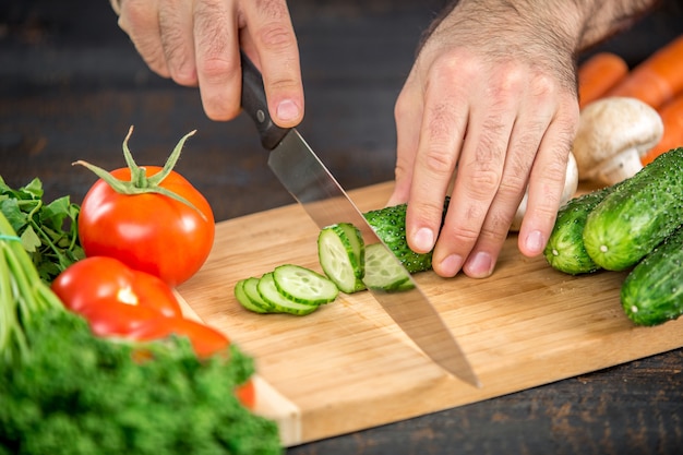 Männliche Hände schneiden Gemüse für Salat