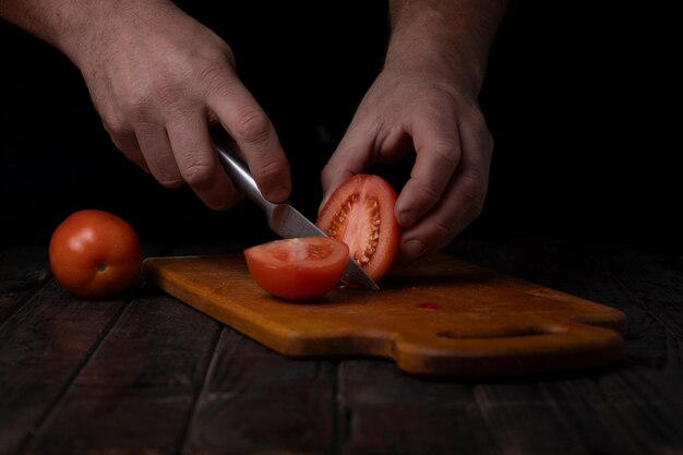 Männliche Hände schneiden Tomaten auf einem Schneidbrett