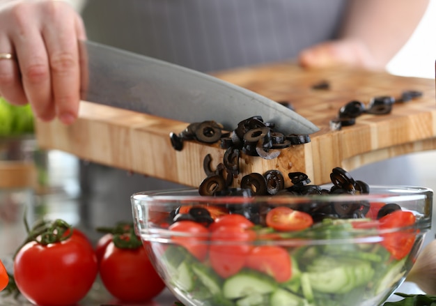 Männliche Hände setzen schwarze Olivenscheiben Glasschale