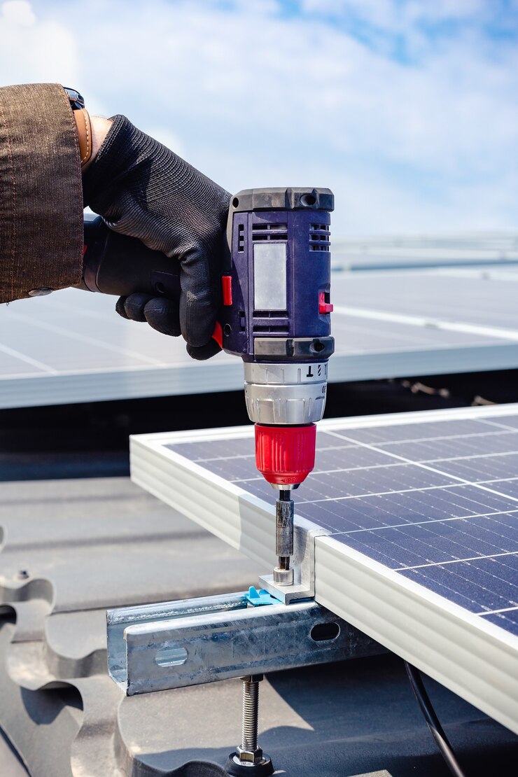 Männliche Hand des Solaringenieurs, die mit Bohrer arbeitet, der Sonnenkollektor auf Hausdach gegen blauen Himmel installiert. Solarenergie macht. Sonnenstrom-Technologie. Stock Foto Sonnenkollektoren.