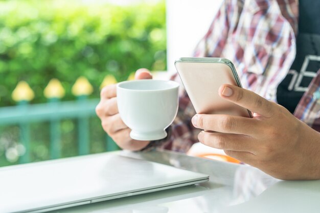 Männliche Hand, die auf dem Tisch intelligentes Telefon und Tasse Kaffee hält