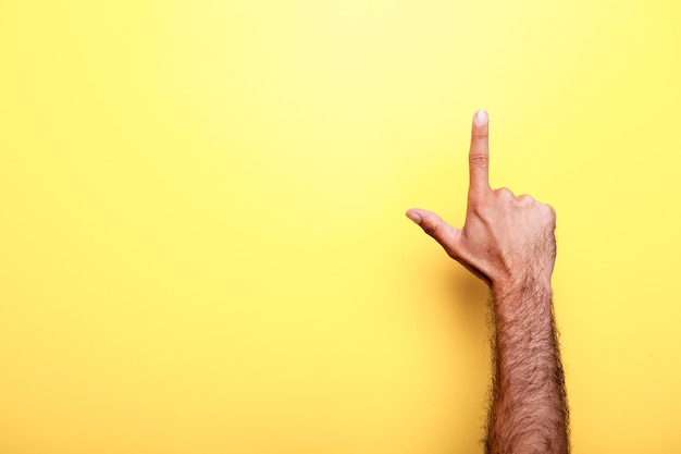 Foto männliche hand, die auf einem gelben hintergrund im studiofoto nach oben zeigt