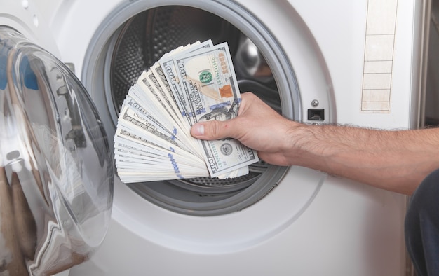 Männliche Hand, die Dollar in der Geldwäsche der Waschmaschine hält