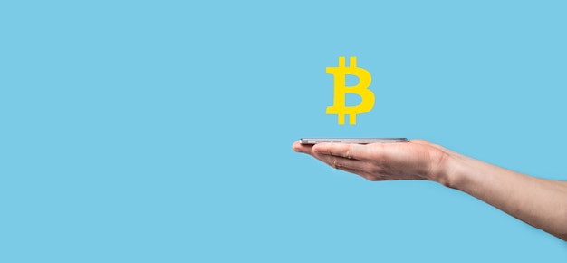 Männliche Hand, die ein Bitcoin-Symbol auf blauem Hintergrund hält. Bitcoin-Kryptowährung Digitale Bitmünze BTC-Währungstechnologie Business Internet Concept.