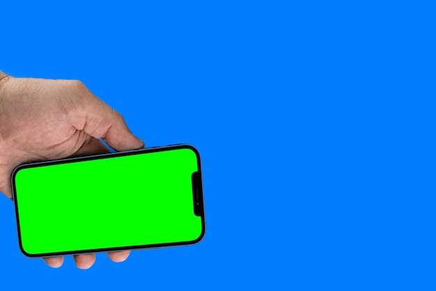 Männliche Hand, die ein Smartphone mit einem grünen Bildschirm hält. Chroma-Key. Auf blauem Hintergrund isoliert.