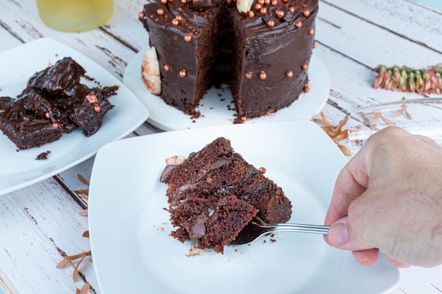 Männliche Hand, die ein Stück Schokoladenkuchenscheibe mit bitterer Ganache-Füllung mit einer Gabel aufhebt