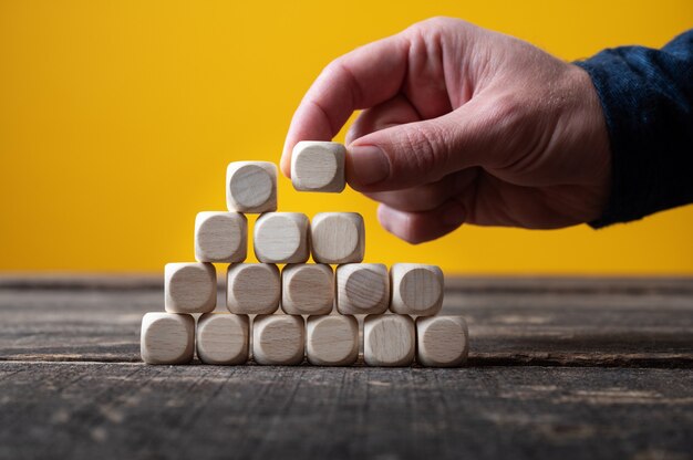 Männliche Hand, die eine Pyramide von hölzernen Würfeln in einem konzeptionellen Bild baut.