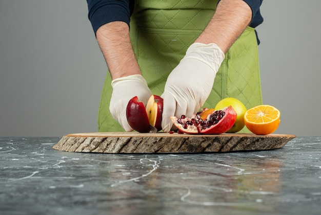 Männliche Hand, die frische rote Äpfel auf Marmortisch schneidet.